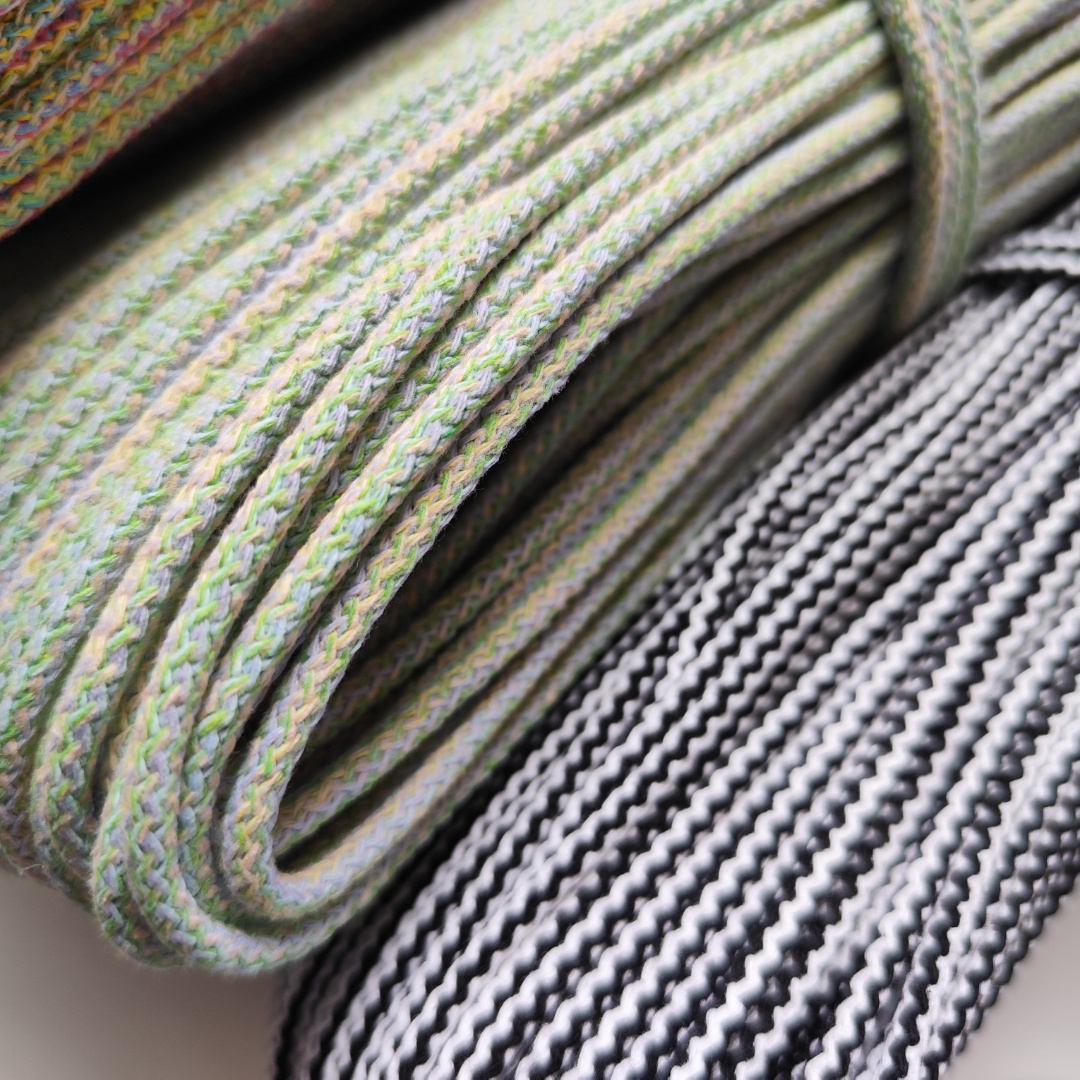 Close-up of rolled braided cords or straps in pastel green with multicolor flecks, alongside a gray and white braided cord, showing texture and weave detail.